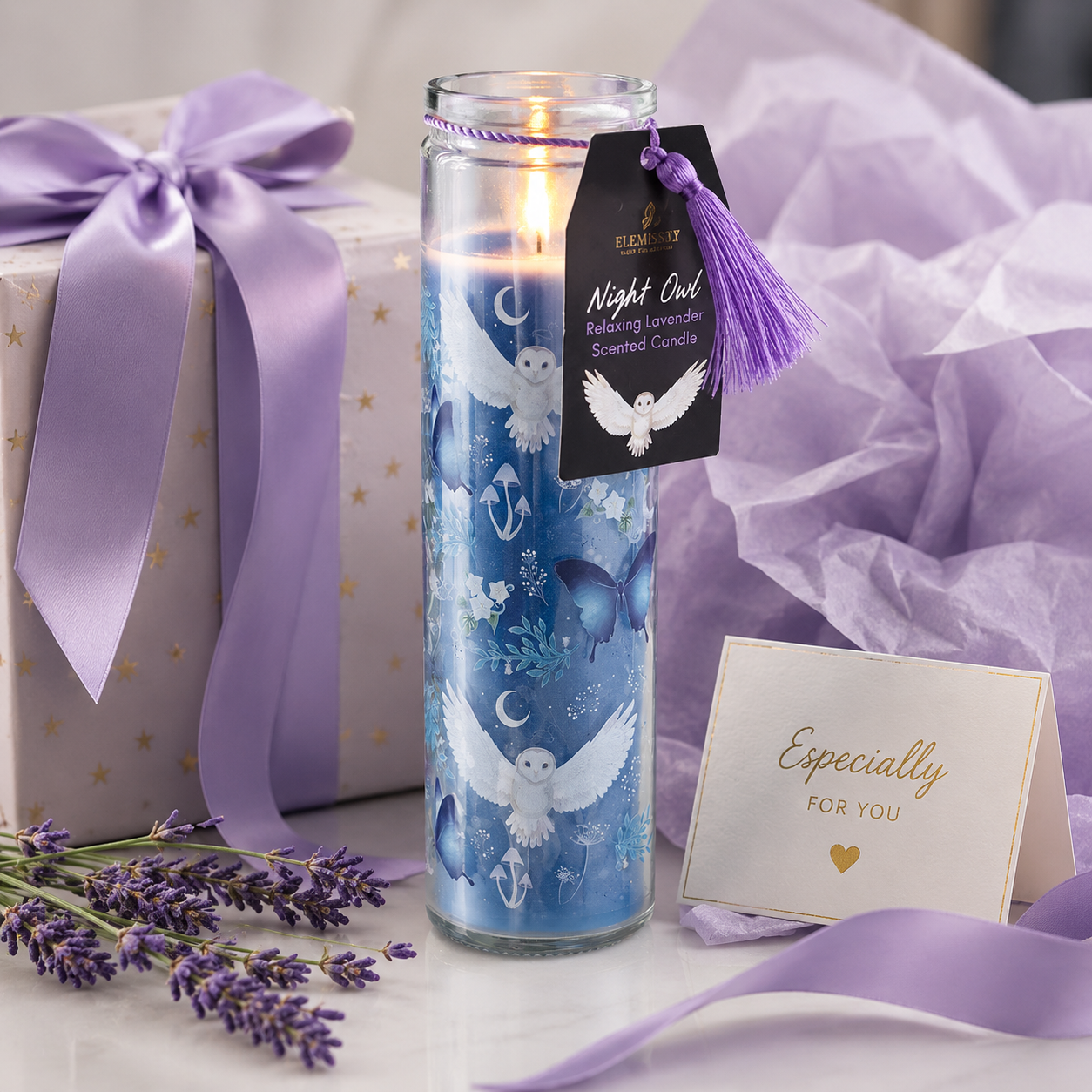 Decorative candle with a tag and gift box on a light surface with lavender flowers.